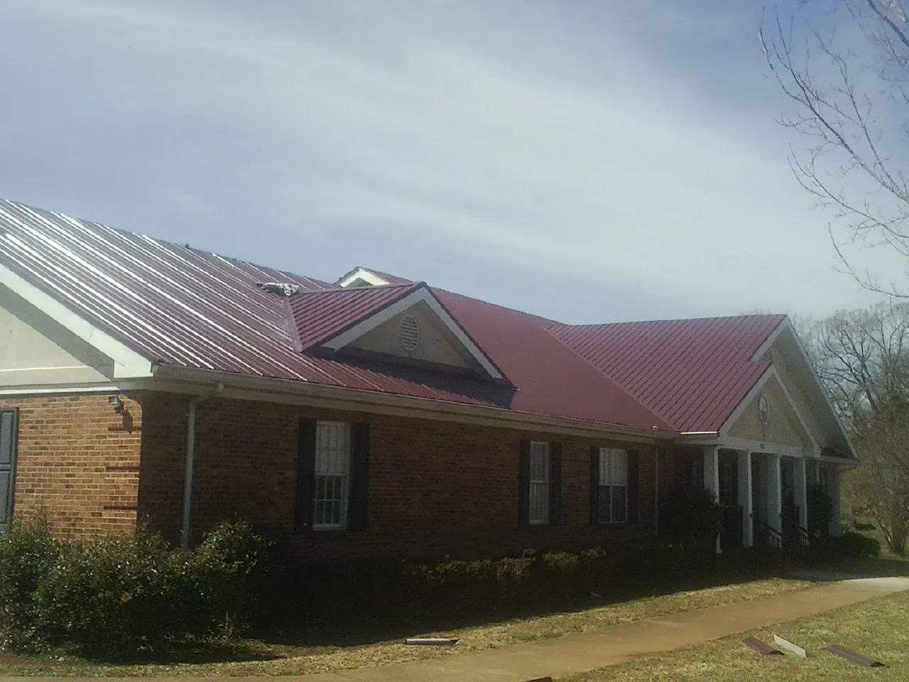 Red metal roof with gabled entries on a long brick building, from a Hail Damage Roof Repair job in Nyssa