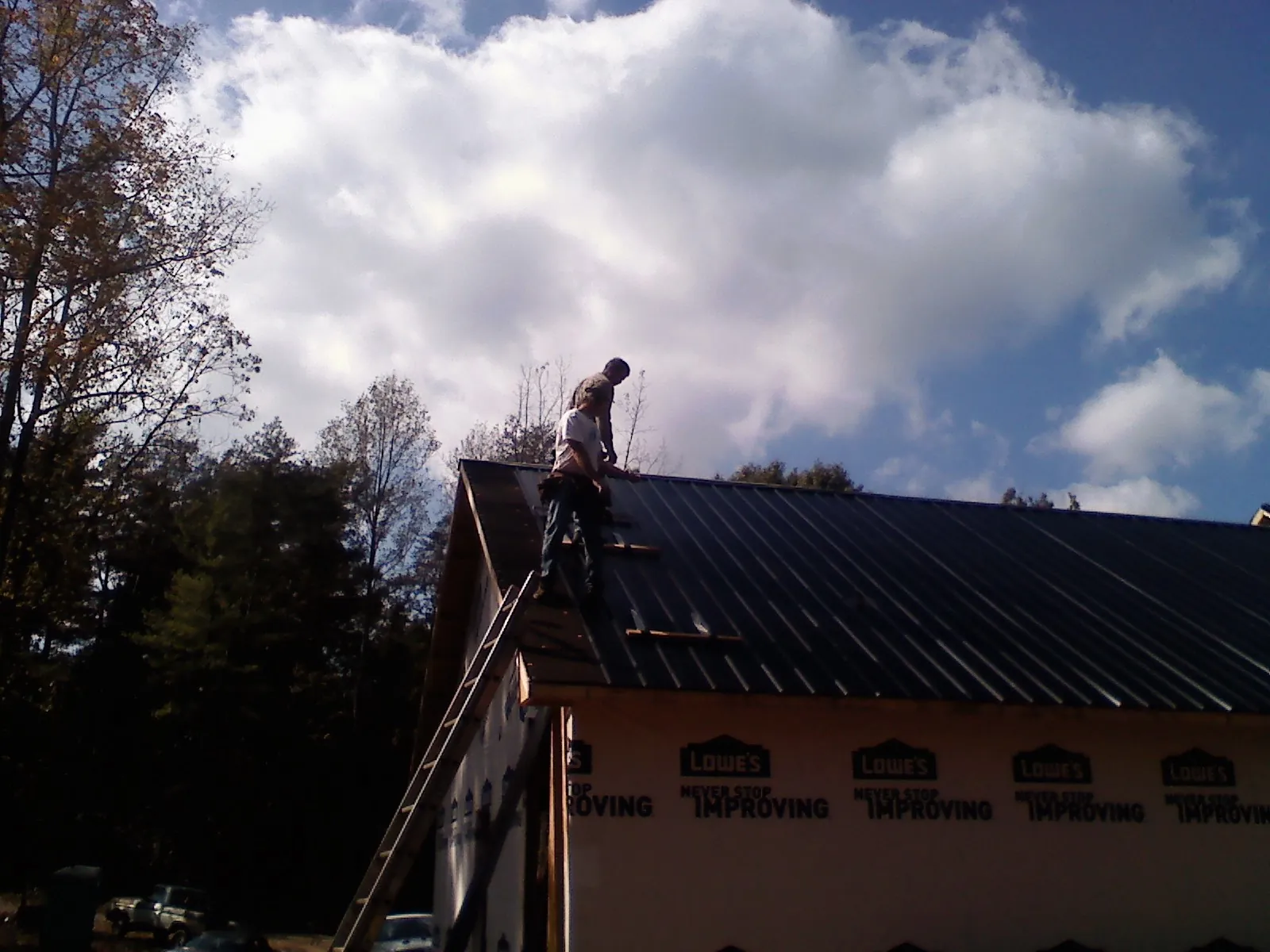 Roofer fastening dark metal panels high against a cloudy sky, from a Roof Inspection job in Nyssa
