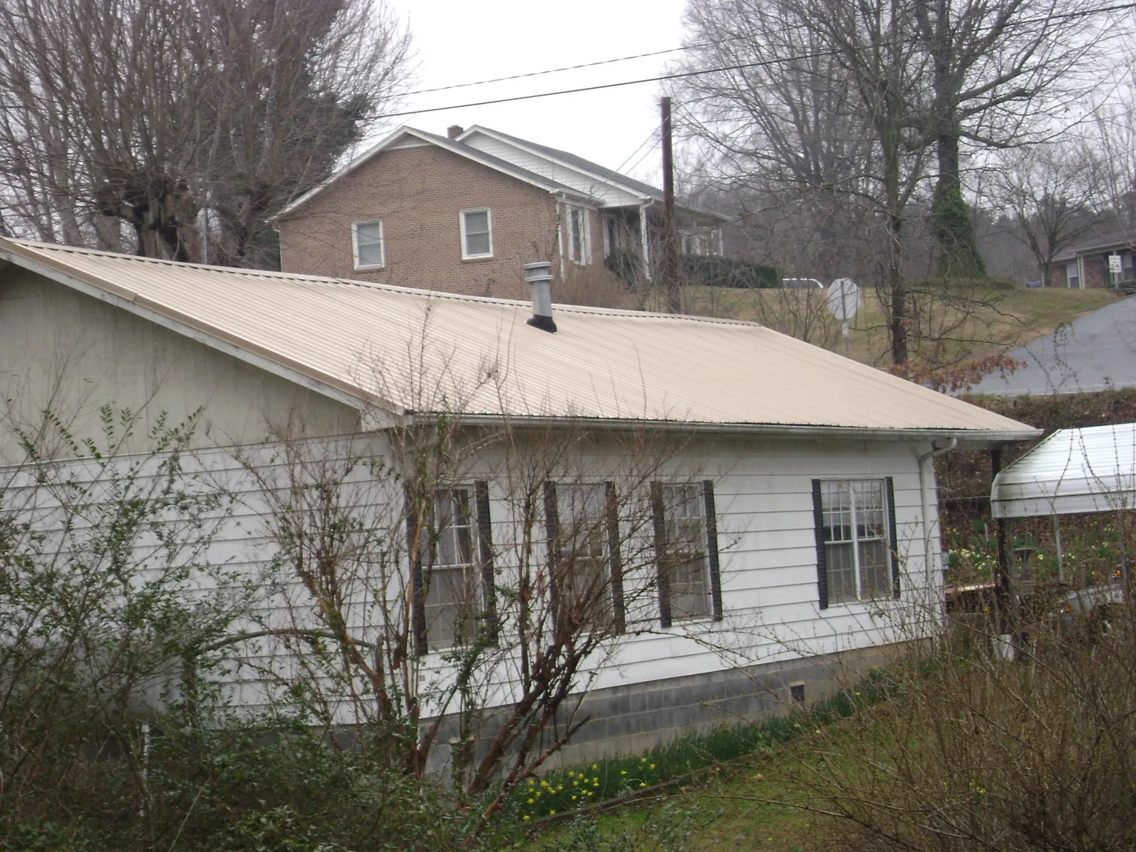 Tan metal roof on a white sided house set into a hillside — Commercial Roofing by Roofing Brothers in Nyssa